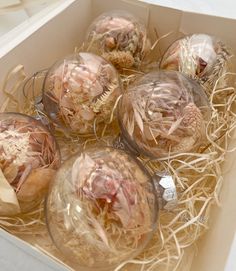 six glass ornaments in a box with straw on the bottom and one is filled with dried flowers