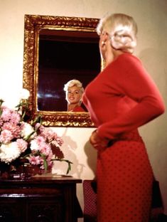 an older woman looking at herself in the mirror with flowers and a vase behind her