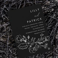 a black and white wedding card with flowers on it sitting in the middle of some sticks