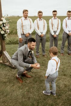 a man kneeling down next to a little boy in front of some other men wearing ties