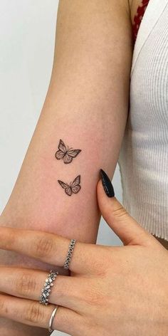 a woman's left arm with three butterflies on the wrist and one is black