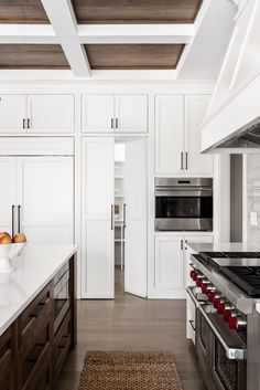 a large kitchen with white cabinets and wood accents on the ceiling, along with an area rug that matches the hardwood flooring