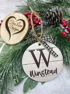 a wooden ornament with the word w on it next to pine cones and berries