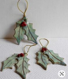 two ceramic holly leaf ornaments with red berries hanging from hooks on a white tablecloth