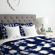 a bed with blue and white comforter in a bedroom next to a clock on the wall