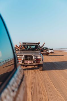 people are riding in the back of a pick up truck on a sandy road near the ocean