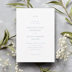 the wedding stationery is laid out on top of some white flowers and greenery