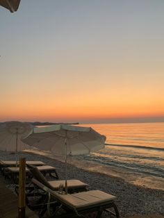 several lounge chairs and umbrellas are on the beach at sunset, with an ocean in the background