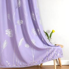 a purple curtain with white flowers on it in front of a wooden table and chair