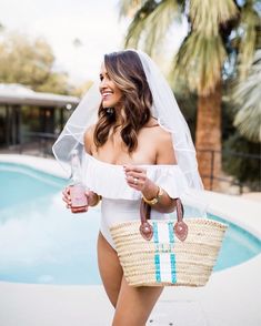 a woman holding a straw bag next to a pool