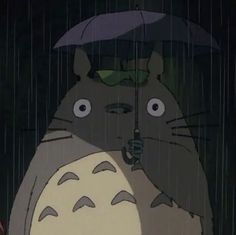 a person holding an umbrella in the rain with a totoro sitting on top of it