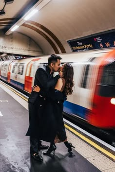 a man and woman standing next to each other in front of a train at a subway station