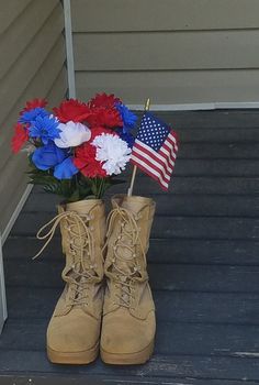 a pair of boots with flowers in them sitting on the steps next to an american flag