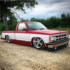 a red and white truck parked on top of a dirt road next to a tree