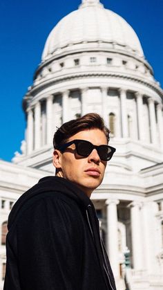 a man wearing sunglasses standing in front of the capital building with his hand on his hip