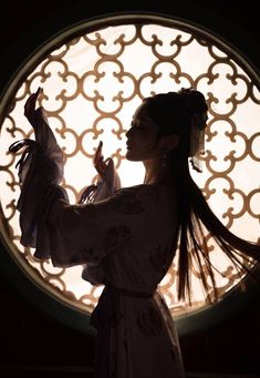 a woman with long hair standing in front of a circular window holding something up to her face