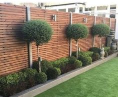 a wooden fence with trees and bushes in the front yard, along with artificial grass