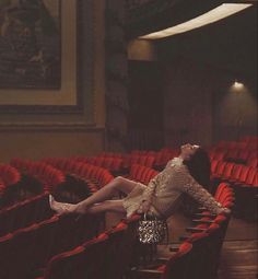 a woman sitting in an empty theater with her legs up on the seats and looking up