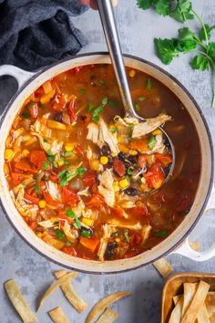 a pot filled with chicken tortilla soup next to chips and cilantro