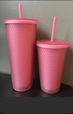 two pink cups sitting on top of a table next to each other with straws in them