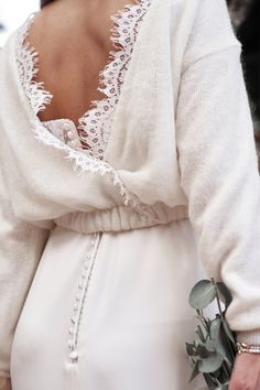 the back of a woman's white dress with lace on it and flowers in her hand