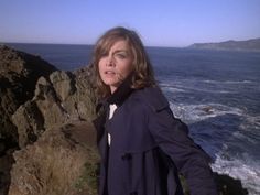 a woman standing on top of a cliff next to the ocean