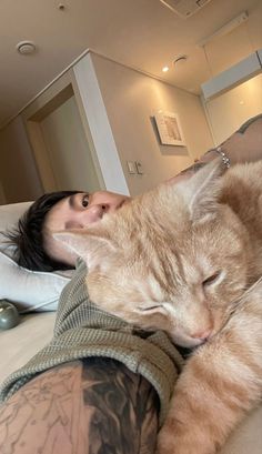 a woman laying on top of a bed next to an orange and white cat with her eyes closed