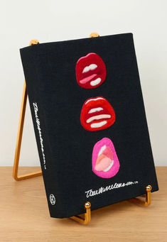 an easel with three lipstick prints on it sitting on top of a wooden table