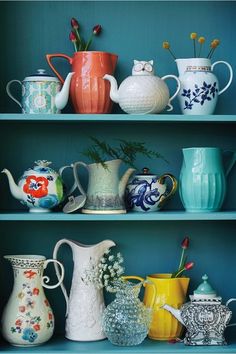 several vases and pitchers are on the shelves in this blue room with teal walls