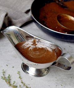 there is a sauce being poured into a bowl with spoons on the table next to it