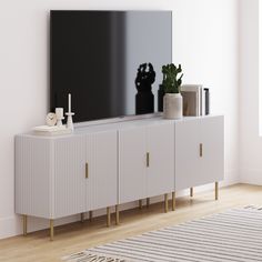 a white entertainment center with a black television on it's stand and a potted plant next to it