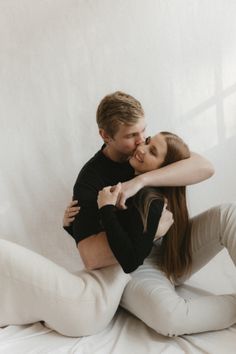 a man and woman sitting on top of each other in white pants, posing for the camera