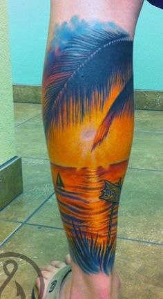 a man's leg with a palm tree and sunset on the beach tattoo design