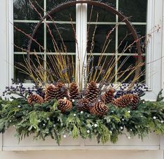 a window sill decorated with pine cones, berries and greenery in front of a circular window