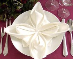 a white plate with napkins and silverware is on a purple table cloth next to wine glasses