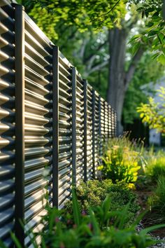 an outdoor garden with green plants and bushes next to a fence that is lined with metal slats