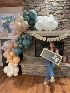 a woman holding a chalkboard standing in front of a fireplace with balloons all around her