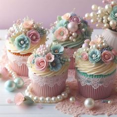 cupcakes decorated with pastel flowers and pearls on a lace doily next to a vase