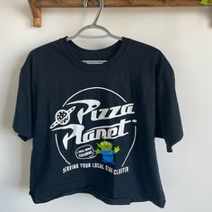 a pizza planet t - shirt hanging on a wooden rack next to a green plant