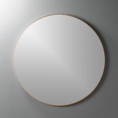 a round mirror hanging on the wall next to a gray wall with a gold frame