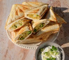 several pita sandwiches on a white plate next to a bowl of sour cream sauce