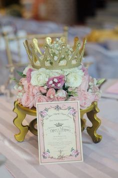 a table topped with pink and white flowers next to a gold crown on top of a card