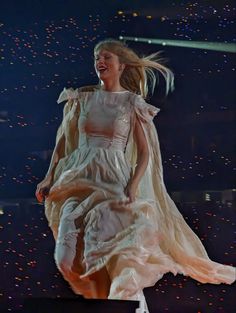 a woman in a white dress is walking on a stage with her hair blowing in the wind