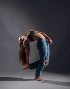 a woman in jeans is doing a handstand on her head and arms with one hand