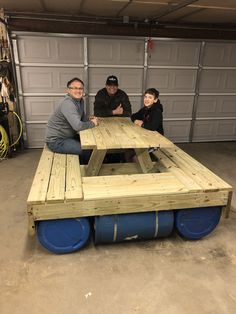 three people sitting at a picnic table made out of pallet boards in a garage