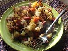 a green plate topped with meat and vegetables on top of a colorful table cloth next to a fork