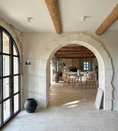 an arched doorway leads to a dining room and living area with stone walls, exposed beams and flooring