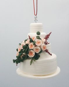 a white wedding cake with pink roses on top hanging from a red string and attached to a silver ornament