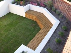 a wooden bench sitting on top of a lush green field next to a brick wall