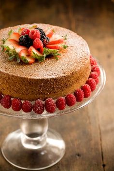 a cake with berries and strawberries on top sits on a glass stand, ready to be served